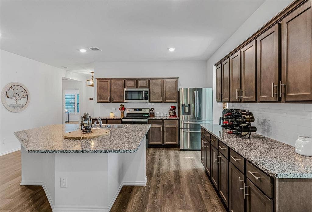 118 Secretariat Lane, Caddo Mills, TX 75135 Kitchen with dark brown cabinets, an island with sink, dark hardwood / wood-style flooring, light stone countertops, and stainless steel appliances