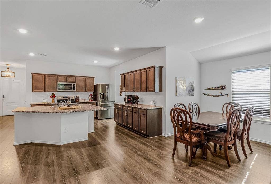 118 Secretariat Lane, Caddo Mills, TX 75135 Kitchen with lofted ceiling, a kitchen island with sink, dark hardwood / wood-style floors, appliances with stainless steel finishes, and light stone counters