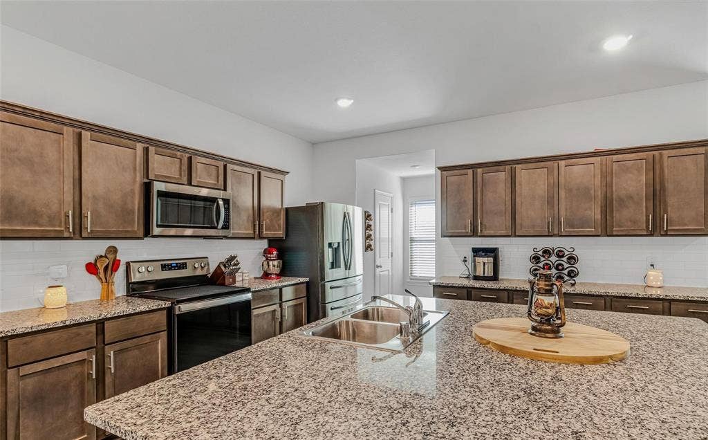 118 Secretariat Lane, Caddo Mills, TX 75135 Kitchen with decorative backsplash, stainless steel appliances, dark brown cabinets, sink, and light stone counters