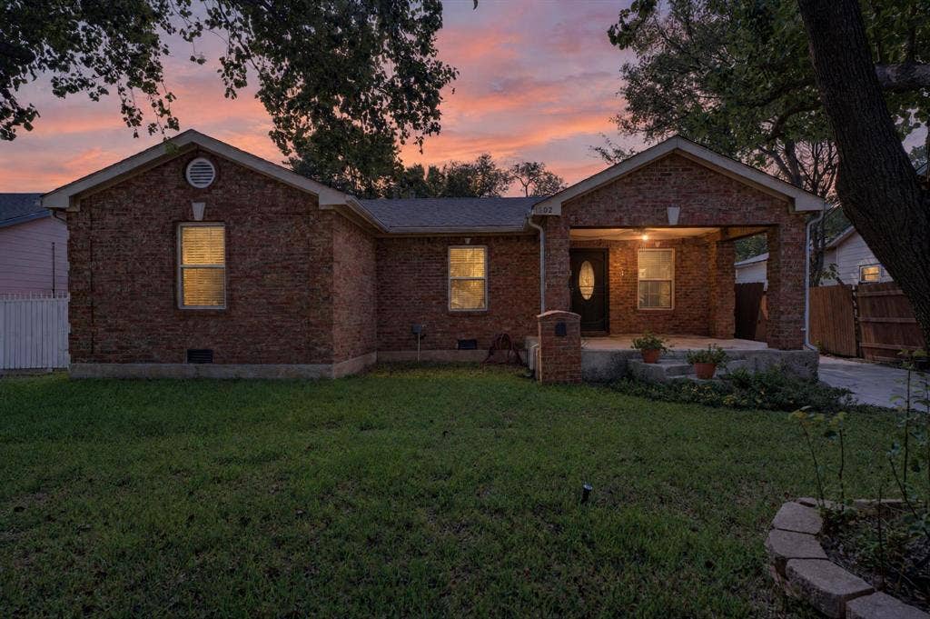 Sunset setting of the brick exterior featuring a covered front porch, gabled roofline, and front lawn with stone border
