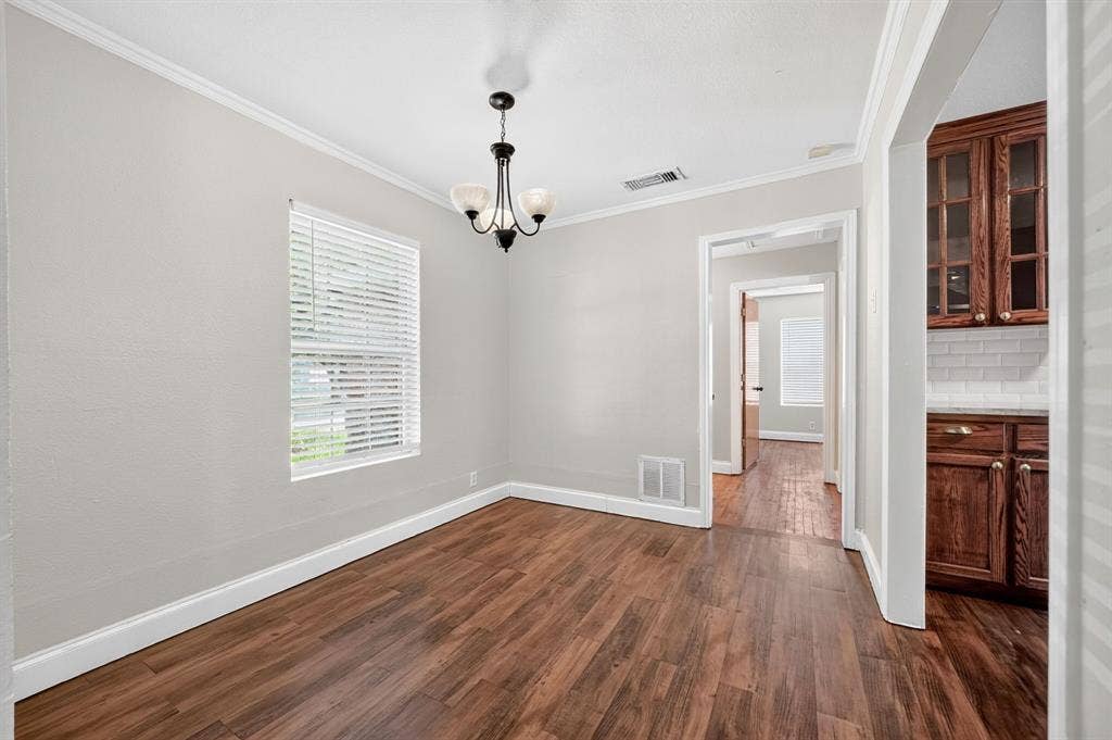Neutral-toned walls featuring crown molding, wood-finish flooring, and a multi-arm pendant light fixture