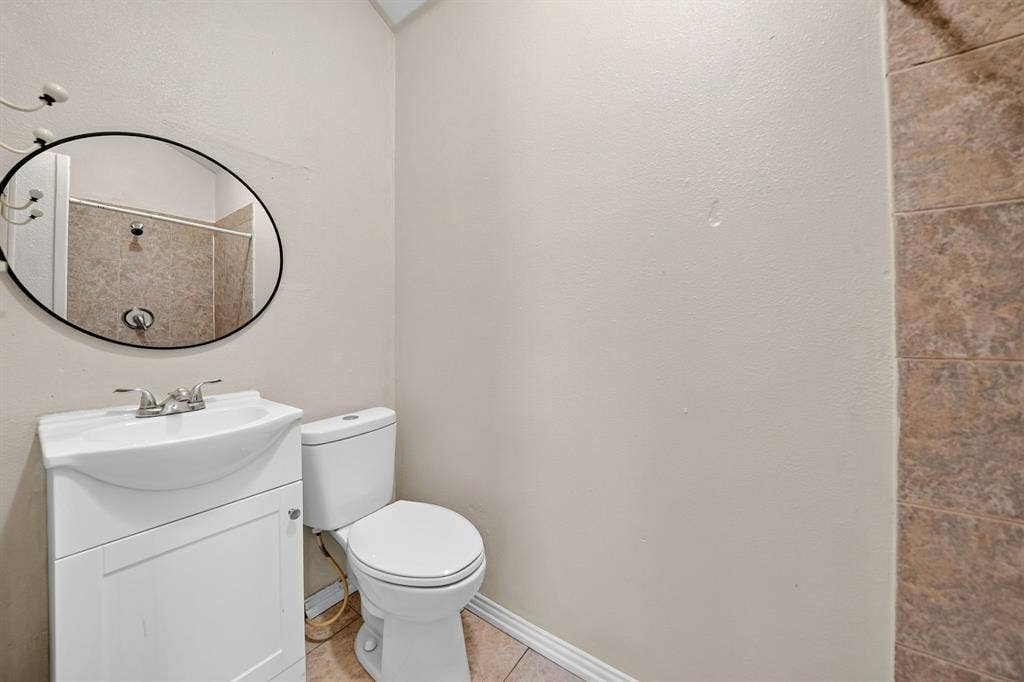 Bathroom featuring a white vanity cabinet with an integrated basin, oval wall-mounted mirror, ceramic tile flooring, and a tiled shower surround