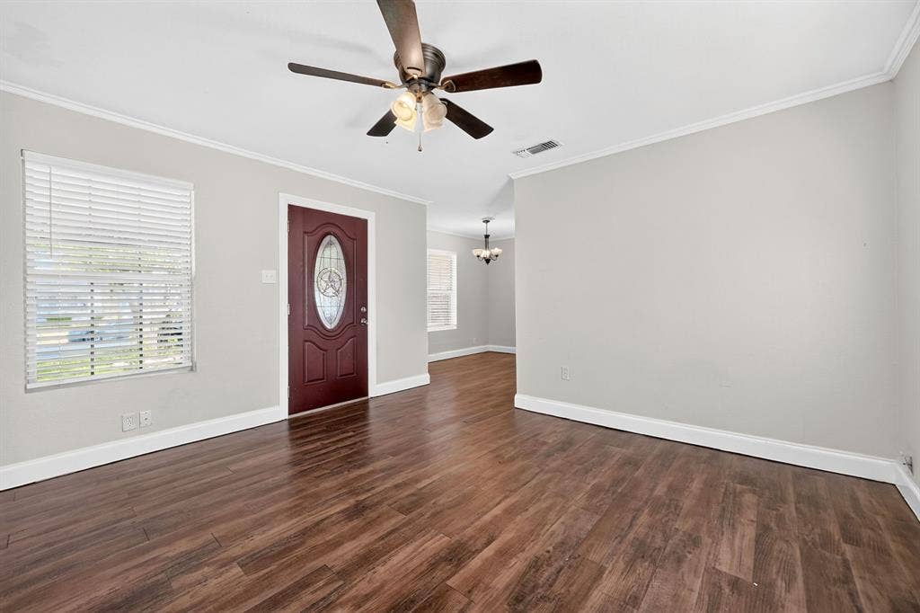 Wood-finish flooring, ceiling fan with integrated light fixture, mahogany entry door with oval glass inset, and crown molding