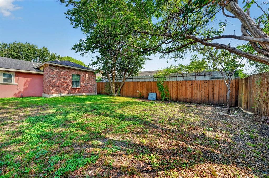 Private backyard featuring a brick exterior wall, mature canopy trees, and full-perimeter wood fencing