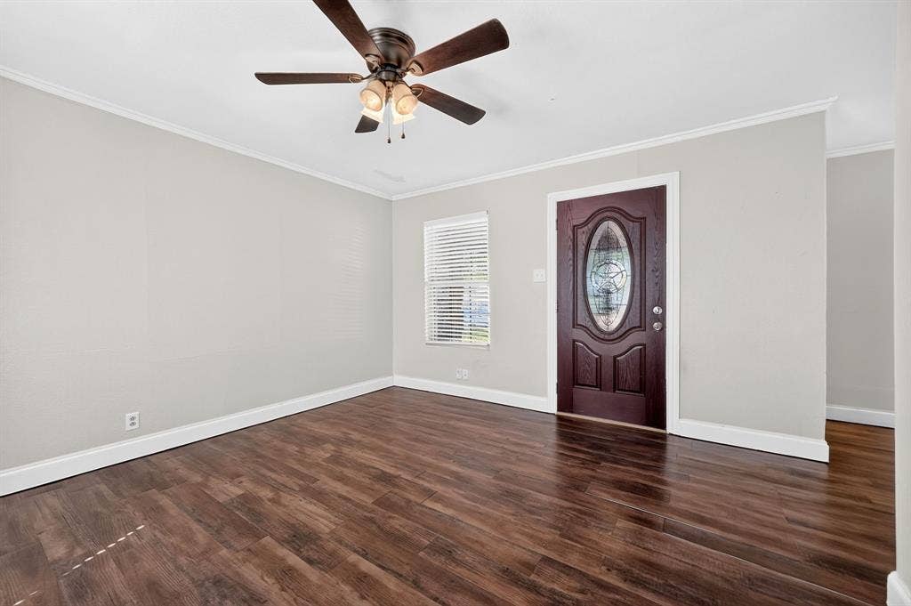 Interior room featuring wood-finish flooring, neutral wall paint, a ceiling fan with integrated lighting, and a front entry door with an oval decorative glass insert