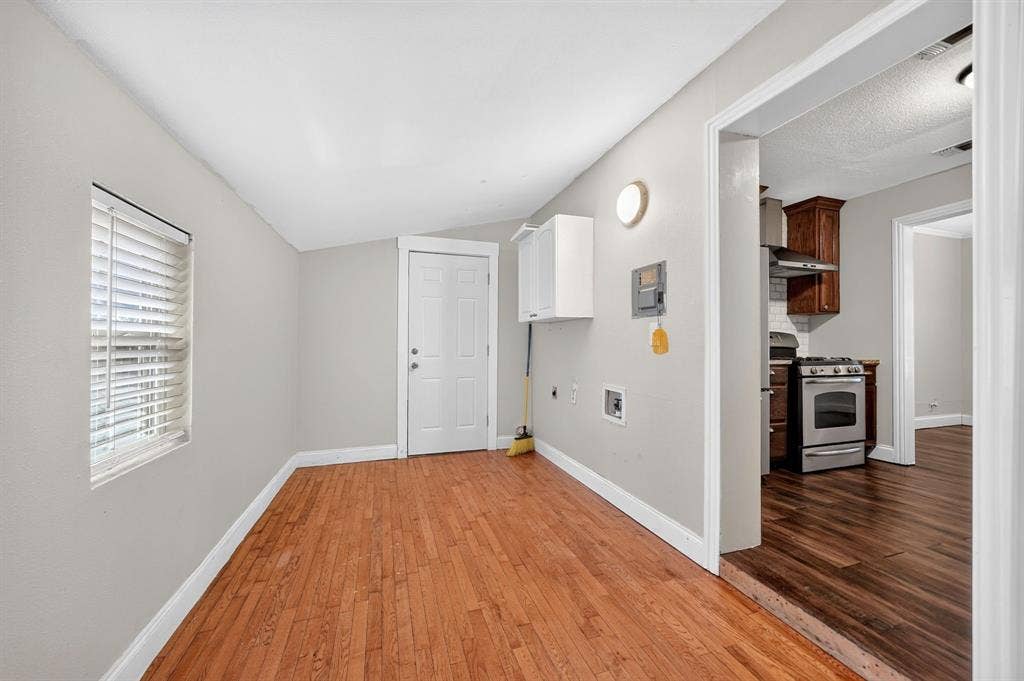 Room featuring wood-finish flooring, white wall-mounted cabinetry, a window with horizontal blinds, and a solid-core door