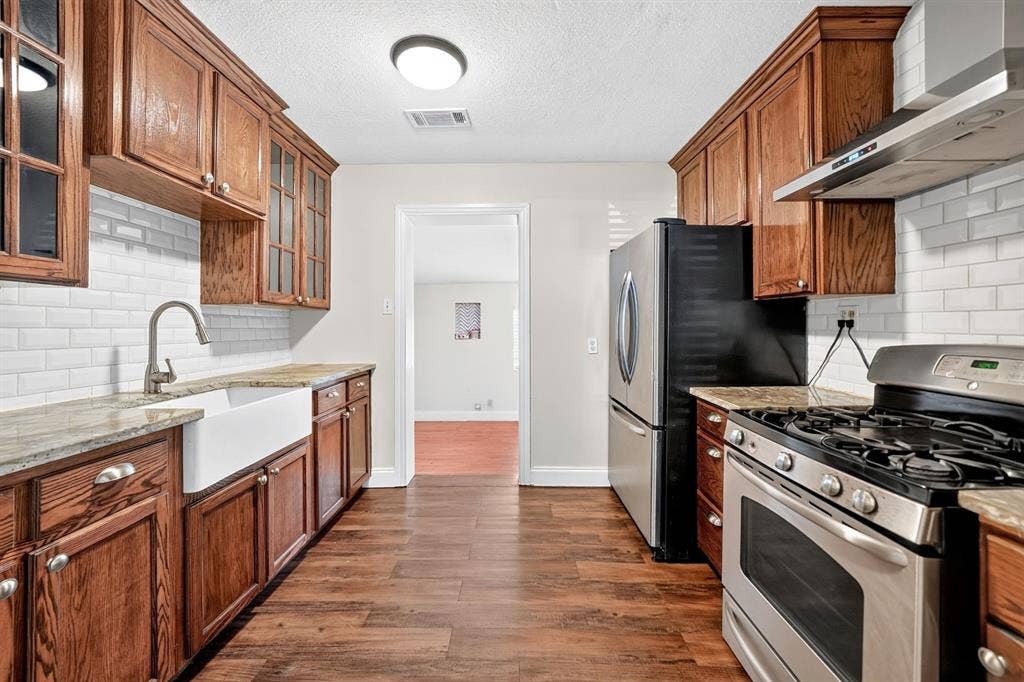 Kitchen featuring stained wood cabinetry, granite countertops, white subway tile backsplash, farmhouse-style sink, and stainless steel gas range