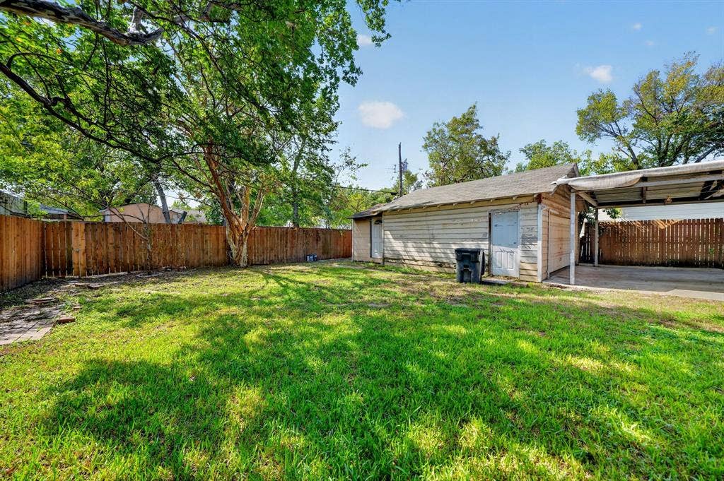 Rear yard featuring a grass lawn, perimeter wood fencing, detached structure, and an attached carport