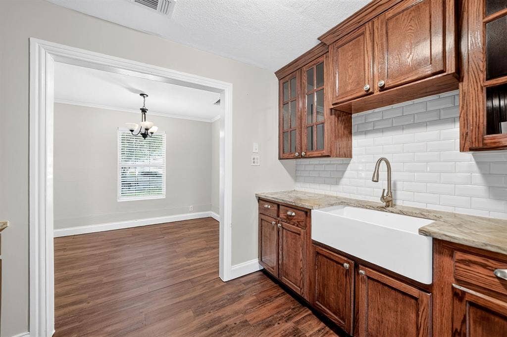 Kitchen featuring stained wood cabinetry with glass-panel upper doors, farmhouse-style apron sink, white subway tile backsplash, and granie countertops