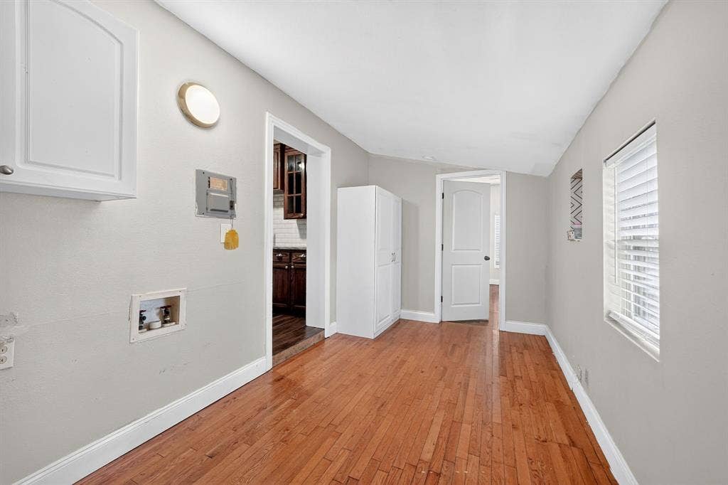 Wood-finish flooring, white upper wall cabinetry, and utility connection box