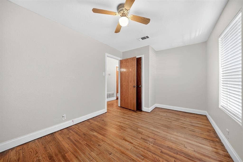 Neutral-toned interior featuring wood-finish flooring, a ceiling fan with light fixture, and horizontal window blinds