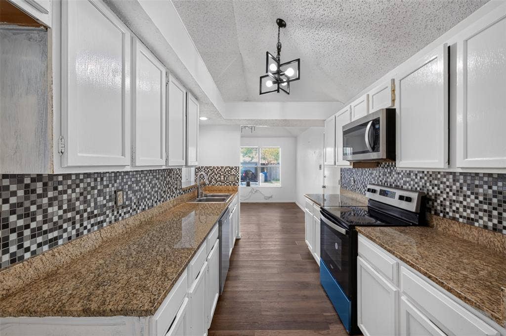 583 Kirkland Drive, Coppell, TX 75019 Galley kitchen featuring white cabinetry, a mosaic tile backsplash, stone-look countertops, stainless steel appliances, and wood-finish flooring