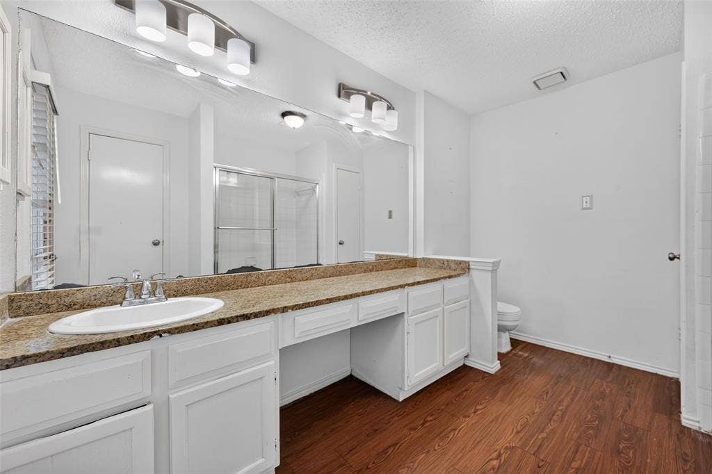 583 Kirkland Drive, Coppell, TX 75019 Dual vanity with a stone-finish countertop, white cabinetry, and wood-finish flooring