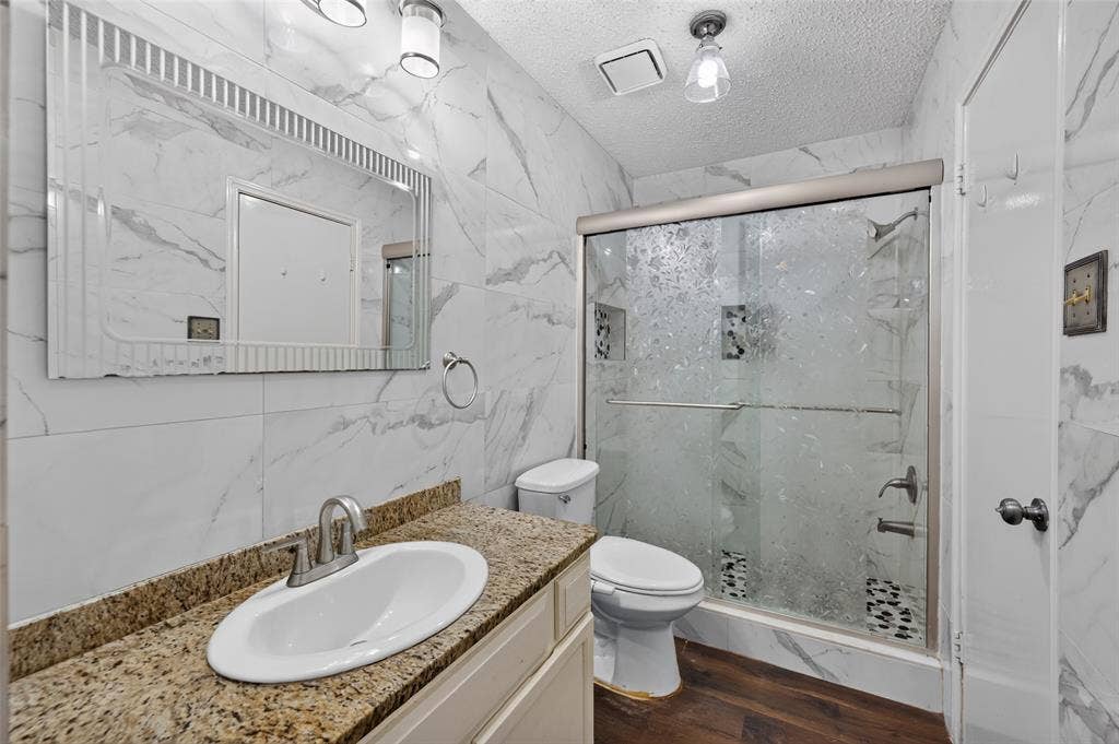 583 Kirkland Drive, Coppell, TX 75019 Full bathroom featuring a shower with a sliding glass door, a vanity with a granite countertop, and wood-finish flooring