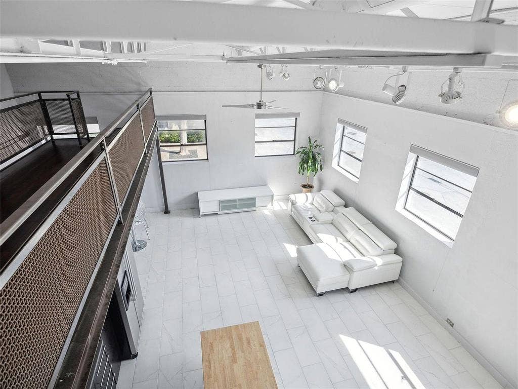 215 N Walton Street, #2, Dallas, TX 75226 Industrial-style loft interior featuring exposed white-painted truss ceilings, large multi-pane windows, polished tile flooring, and a metal mesh mezzanine railing