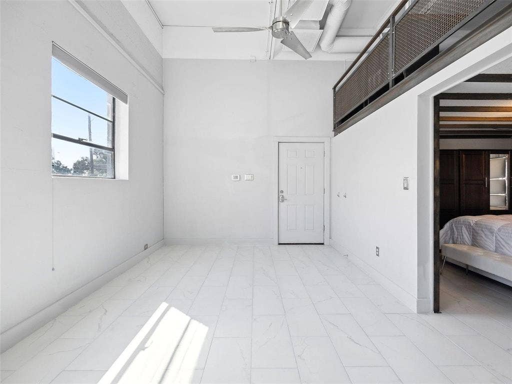 215 N Walton Street, #2, Dallas, TX 75226 High-ceiling industrial loft featuring white tile flooring, exposed ductwork, a metal mesh mezzanine railing, and a ceiling fan