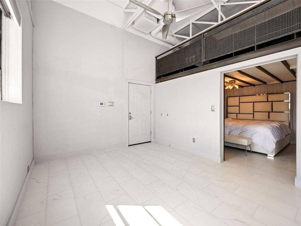 215 N Walton Street, #2, Dallas, TX 75226 High-ceiling industrial interior featuring exposed rafters, a metal mesh loft railing, ceiling-mounted paddle fan, and large-format tile flooring