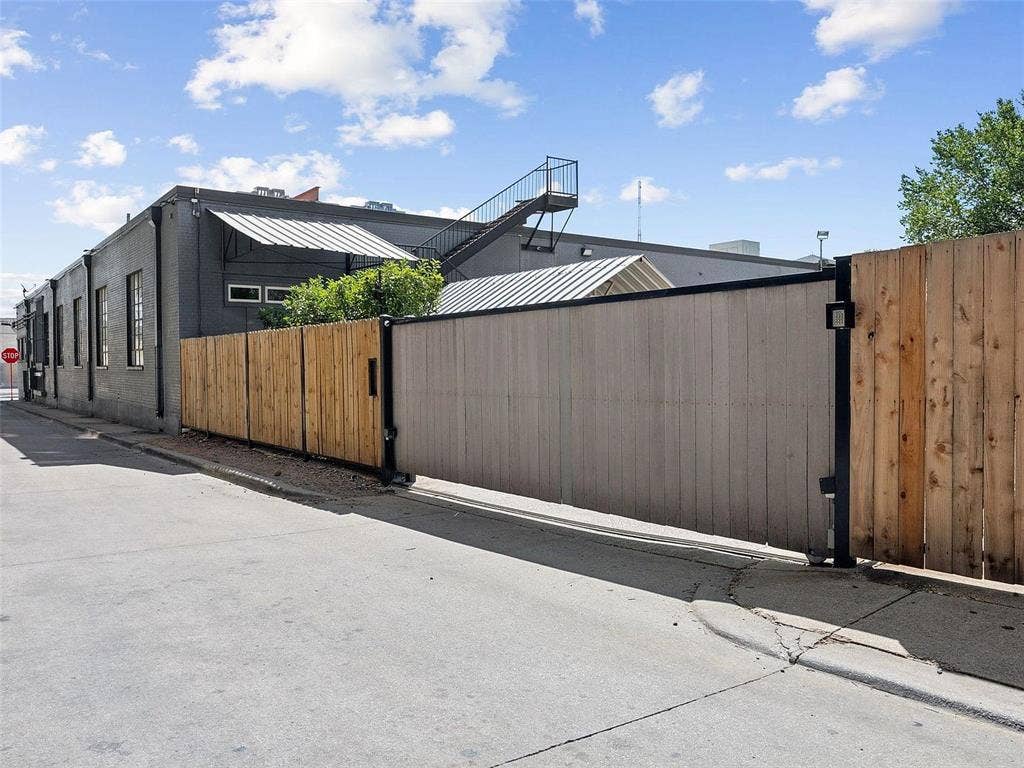215 N Walton Street, #2, Dallas, TX 75226 Exterior view featuring a motorized sliding wood-panel fence, dark-painted masonry siding, metal awning structures, and an exterior steel staircase