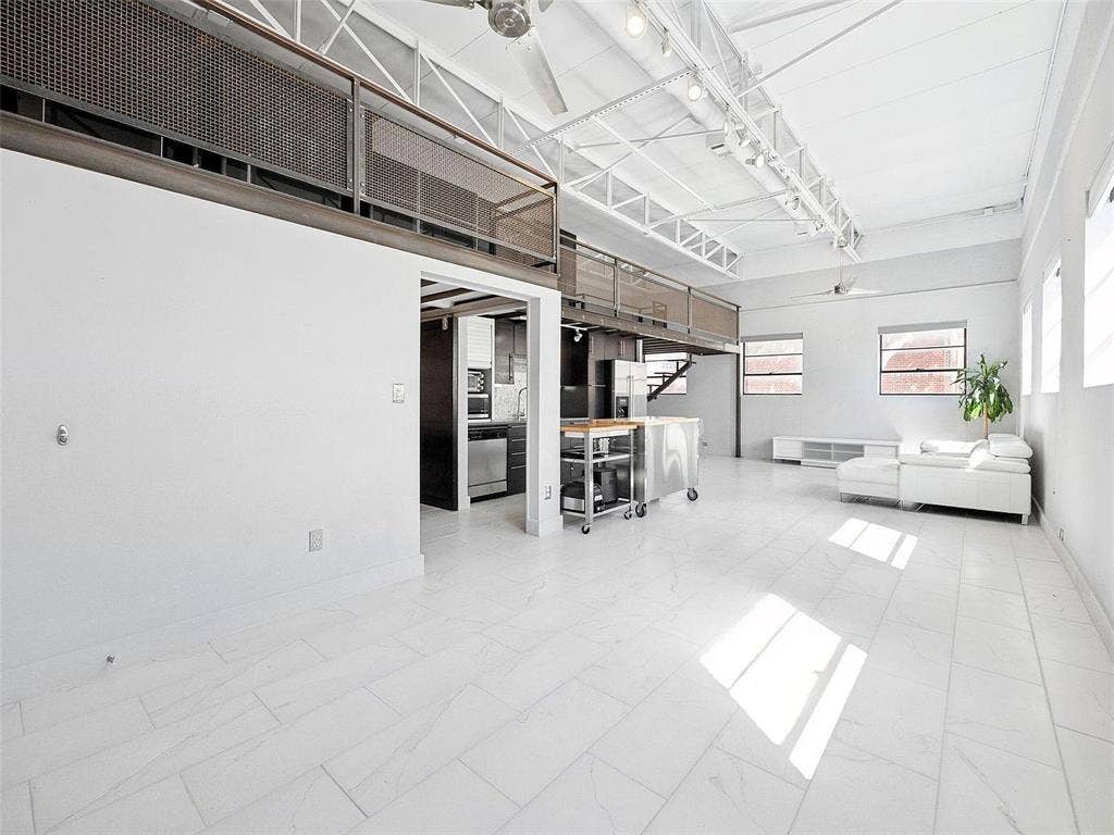215 N Walton Street, #2, Dallas, TX 75226 Industrial-style interior featuring high vaulted ceilings with exposed white trusses, large-format tile flooring, a mezzanine level with decorative metal mesh railing, and track lighting
