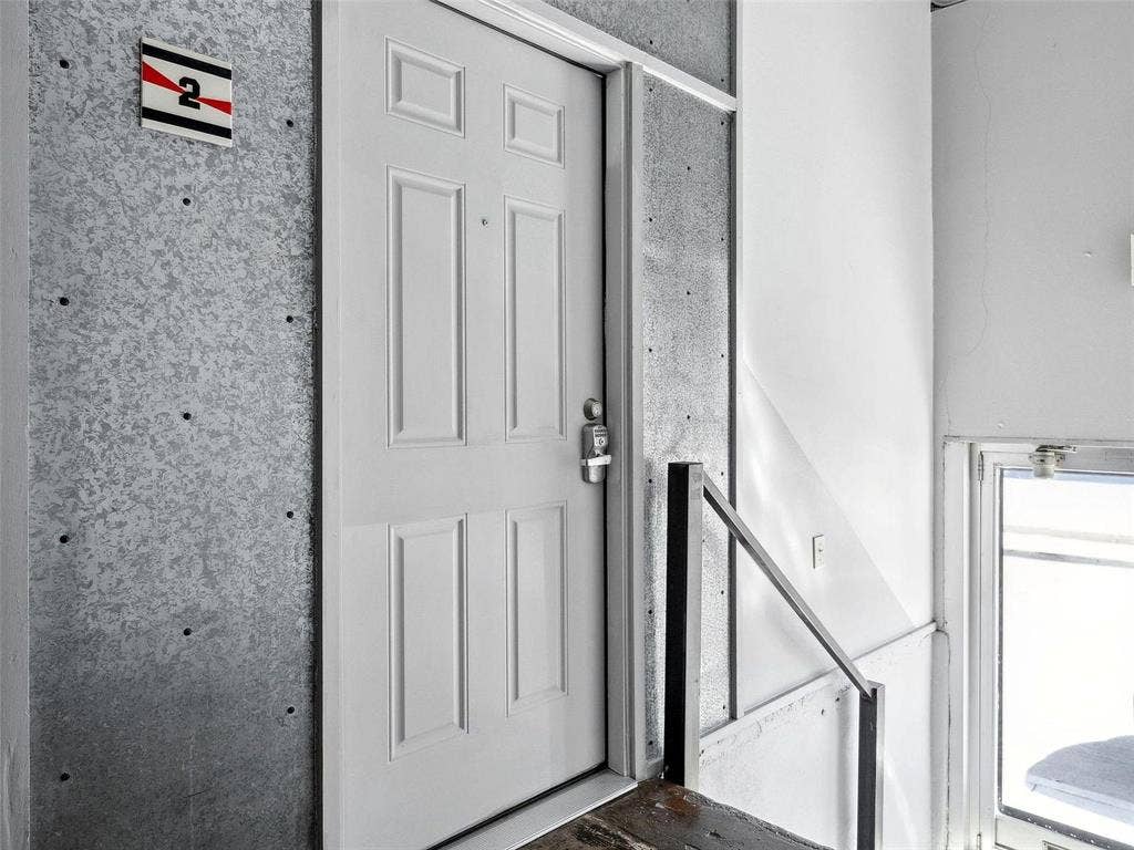 215 N Walton Street, #2, Dallas, TX 75226 Four-panel entry door featuring a brushed metal deadbolt and integrated lock system, set against exposed concrete wall panels with visible mounting hardware and a metal handrail