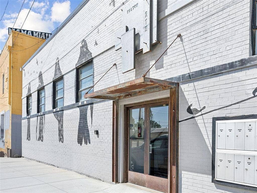 215 N Walton Street, #2, Dallas, TX 75226 Painted brick exterior featuring industrial-style metal awning, glass and metal entrance doors, multi-unit wall-mounted mailbox system, and high-contrast mural detail