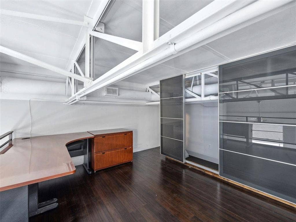215 N Walton Street, #2, Dallas, TX 75226 Industrial-style interior featuring exposed white structural steel trusses, dark wood-finish flooring, and floor-to-ceiling sliding glass storage panels with metal frames