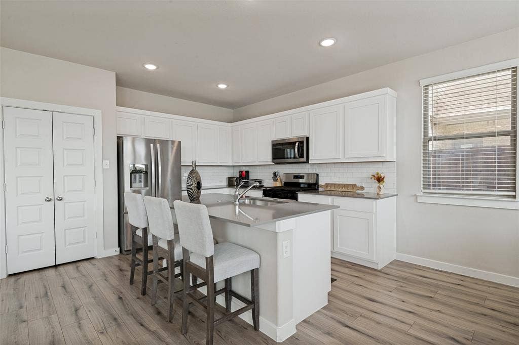 2808 Spring Side Drive, Royse City, TX 75189 Kitchen featuring white cabinetry, solid-surface countertops, subway tile backsplash, stainless steel appliances, and wood-finish flooring