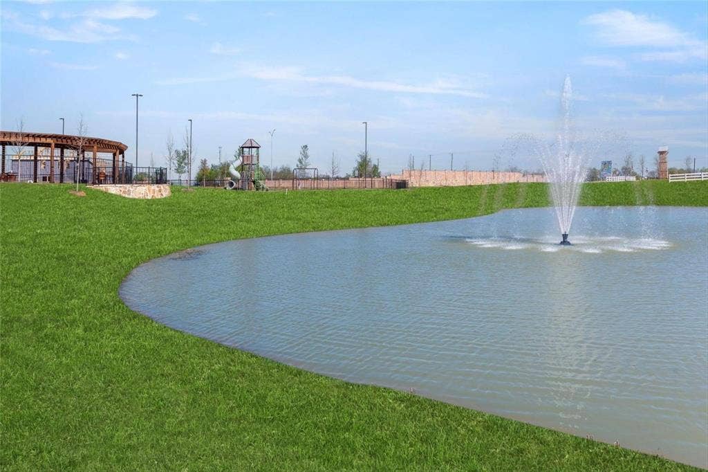 2808 Spring Side Drive, Royse City, TX 75189 Manicured green space featuring a pond with a central fountain, pergola structure, playground equipment, and perimeter stone wall