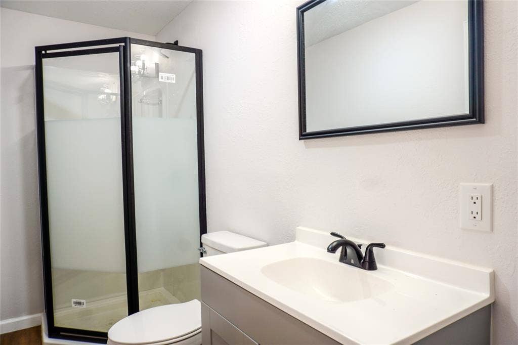 3229 Hardeman Street, Fort Worth, TX 76119 Corner shower enclosure with matte black frame and frosted glass, vanity with integrated basin, matte black faucet, and rectangular wall mirror with a matching black frame