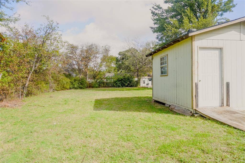 3229 Hardeman Street, Fort Worth, TX 76119 Expansive backyard featuring mature trees, perimeter vegetation, and a detached outbuilding with a wooden ramp entrance