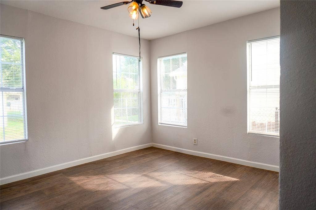 3229 Hardeman Street, Fort Worth, TX 76119 Interior space featuring wood-finish flooring, neutral wall paint, multiple windows with blinds, and a ceiling fan with integrated lighting