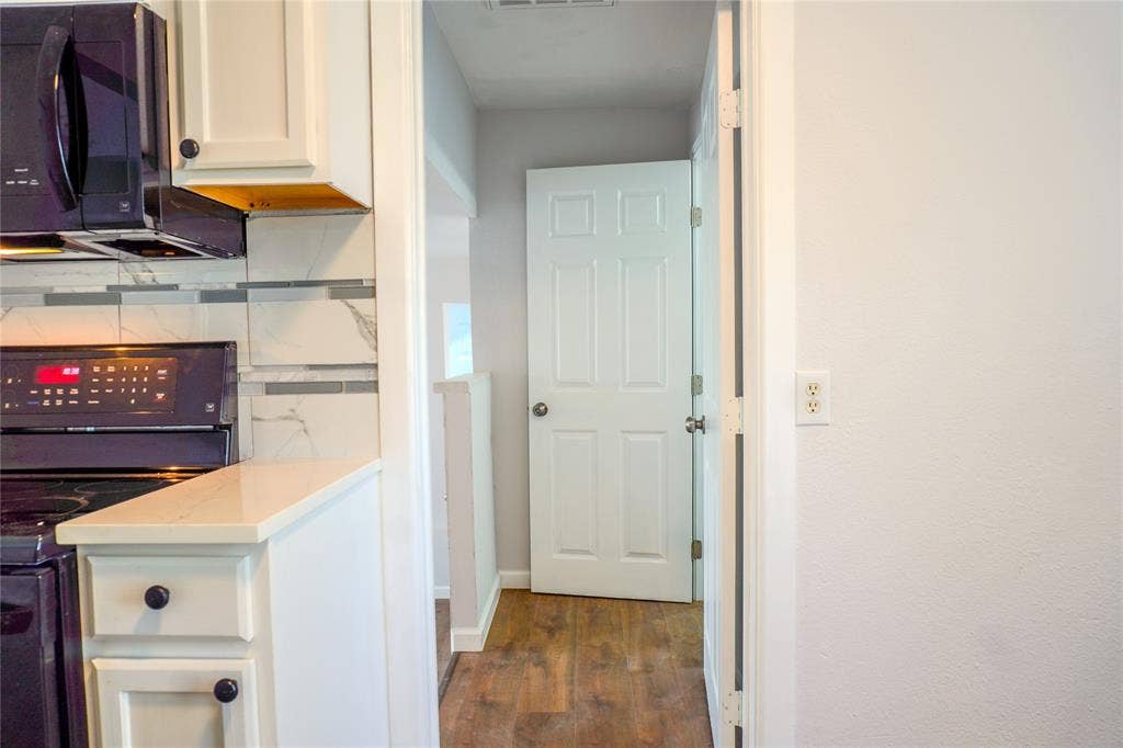 3229 Hardeman Street, Fort Worth, TX 76119 Kitchen featuring white cabinetry, solid-surface countertops, stone-finish tile backsplash, black built-in microwave and range, and wood-finish flooring