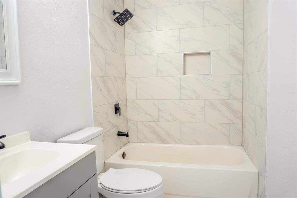 3229 Hardeman Street, Fort Worth, TX 76119 Bathroom featuring a shower-tub combination with light-toned wall tile, a built-in recessed niche, matte black fixtures, and a gray vanity with a white integrated sink