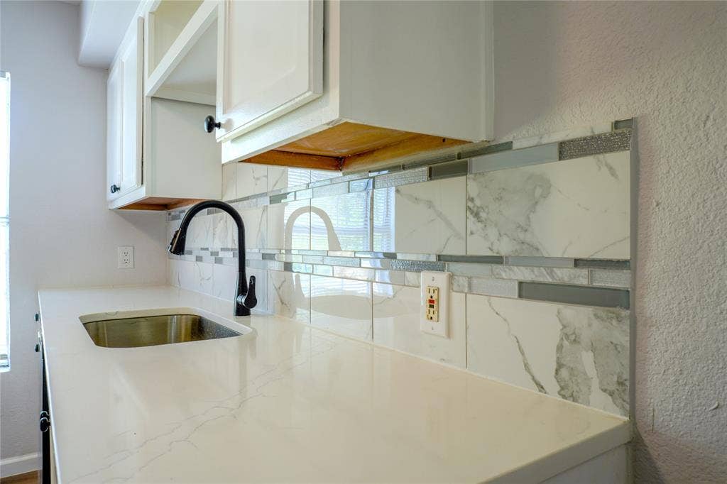 3229 Hardeman Street, Fort Worth, TX 76119 White quartz countertop, undermount stainless steel sink, matte black gooseneck faucet, and decorative tile backsplash featuring large-format stone-patterned tiles accented by glass and metallic horizontal inlay