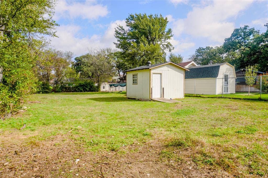3229 Hardeman Street, Fort Worth, TX 76119 Expansive backyard featuring two detached storage structures, chain-link fencing, and mature trees