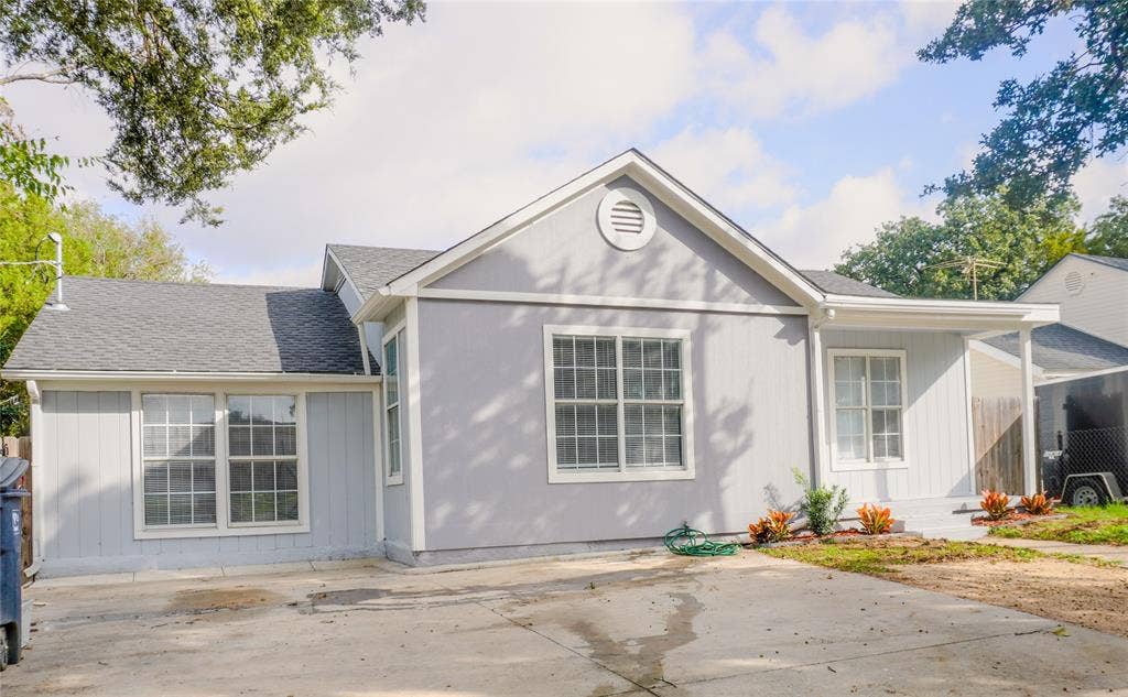 3229 Hardeman Street, Fort Worth, TX 76119 Single-story residence featuring a light gray exterior, vertical siding, gabled roofline, concrete driveway, and covered front entry