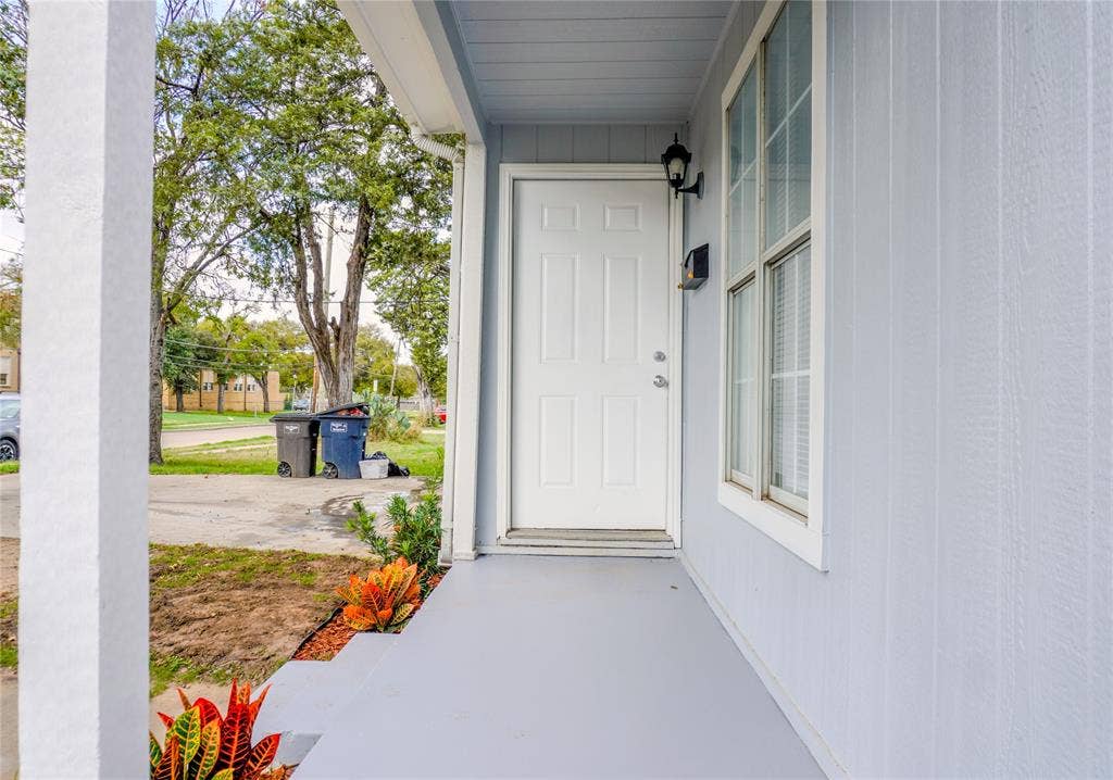 3229 Hardeman Street, Fort Worth, TX 76119 Covered front porch featuring vertical board-and-batten siding, a six-panel entry door, and an exterior wall-mounted lantern light fixture