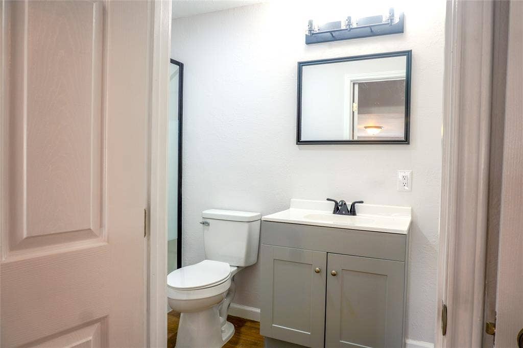 3229 Hardeman Street, Fort Worth, TX 76119 Grey shaker-style vanity with white countertop, integrated sink, matte black faucet, framed vanity mirror, and linear vanity lighting