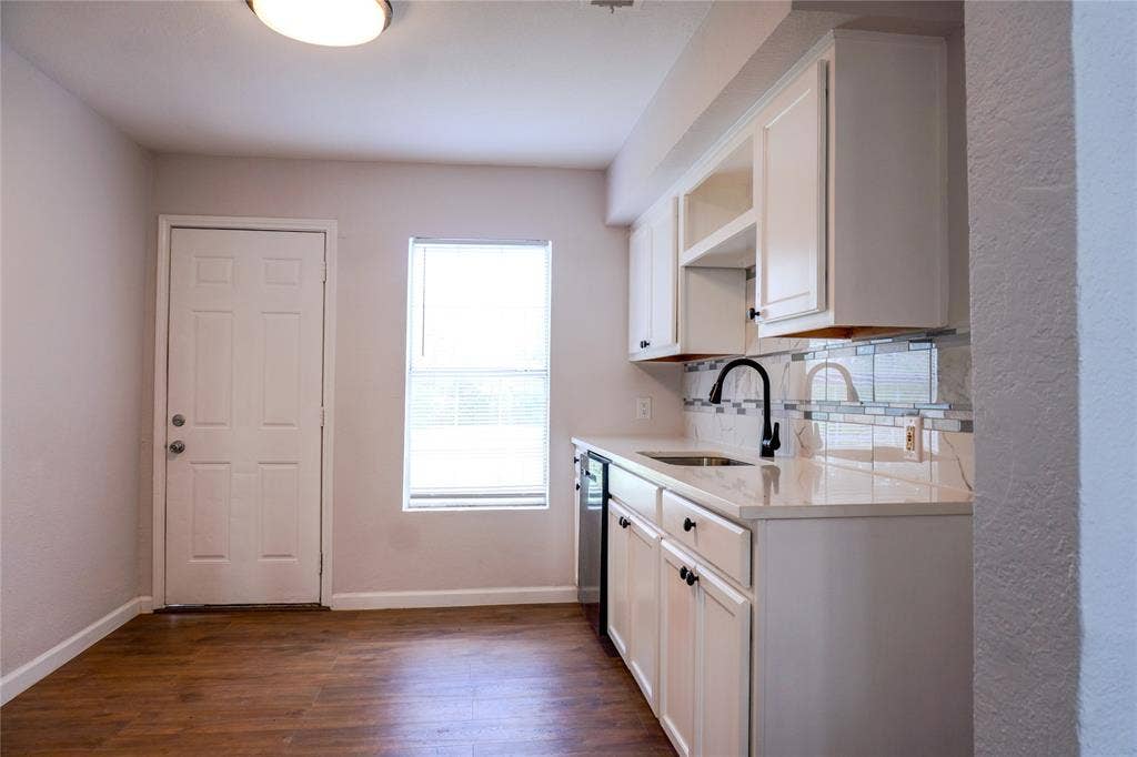3229 Hardeman Street, Fort Worth, TX 76119 Kitchen featuring white cabinetry, light-toned countertops, tile backsplash, wood-finish flooring, and a matte black gooseneck faucet