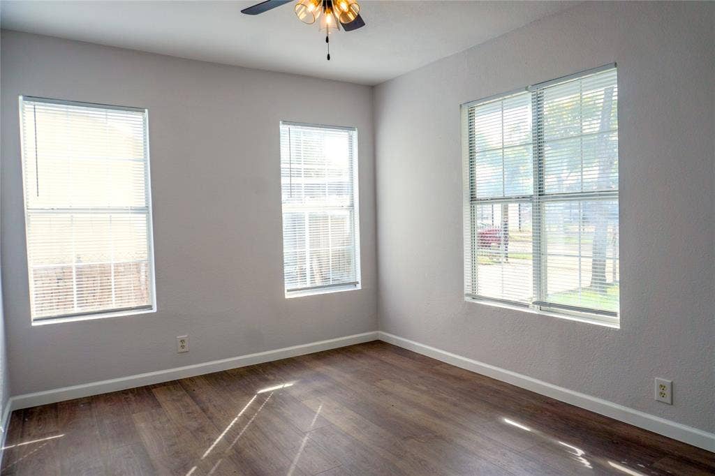 3229 Hardeman Street, Fort Worth, TX 76119 Neutral-toned interior featuring wood-finish flooring, three windows with integrated blinds, and a ceiling-mounted light fixture