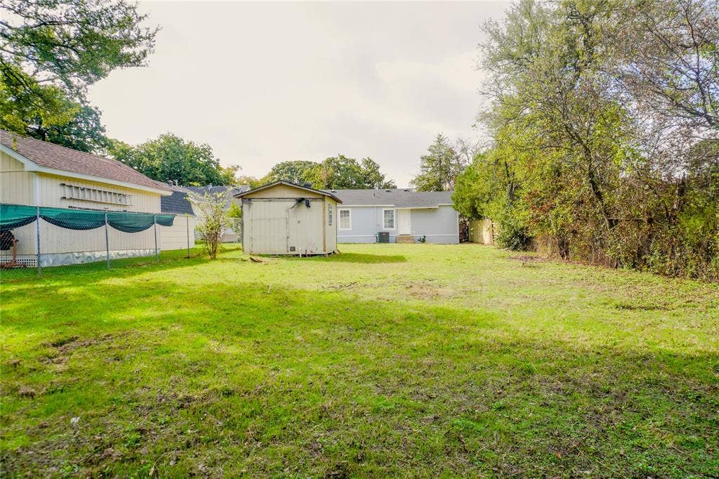 3229 Hardeman Street, Fort Worth, TX 76119 Expansive backyard featuring a lawn, mature perimeter trees, a detached storage structure, and a fenced boundary