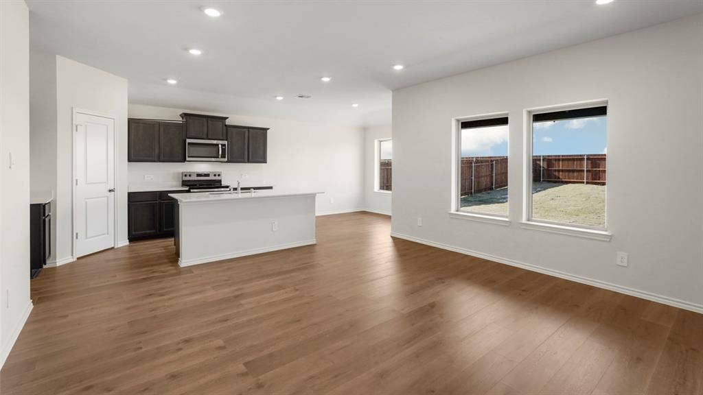 617 Dunham Road, Nevada, TX 75173 Open-concept living area with wood-finish flooring, recessed lighting, and a kitchen featuring dark cabinetry, stainless steel appliances, and a central island