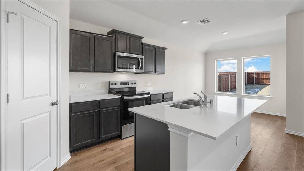 617 Dunham Road, Nevada, TX 75173 Kitchen featuring dark wood-finish cabinetry, stainless steel appliances, a white island with an integrated double sink, wood-finish flooring, and recessed lighting
