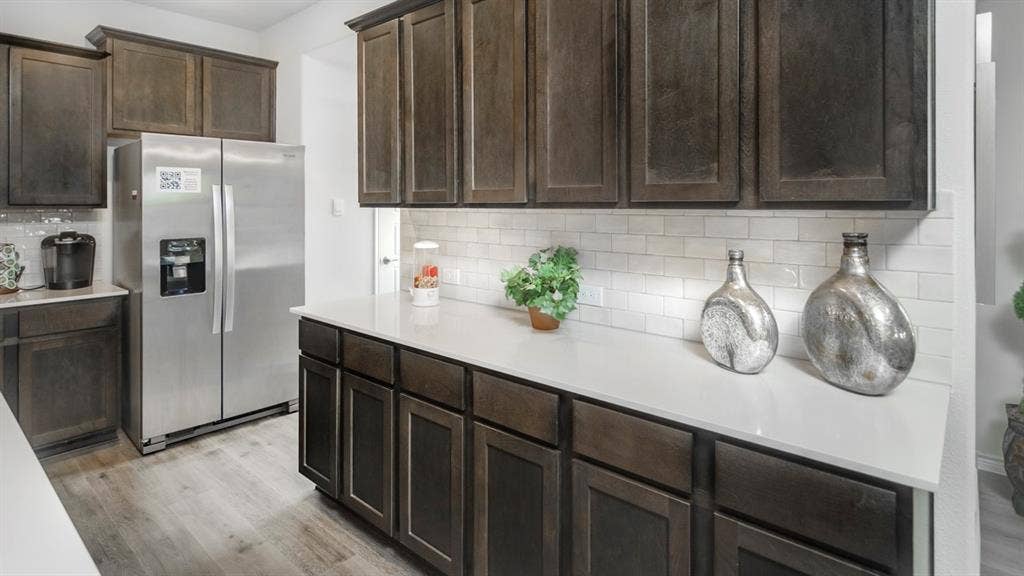 406 Campfield Drive, Caddo Mills, TX 75135 Kitchen featuring dark wood-finish cabinetry, light-toned countertops, subway tile backsplash, stainless steel refrigerator, and wood-finish flooring