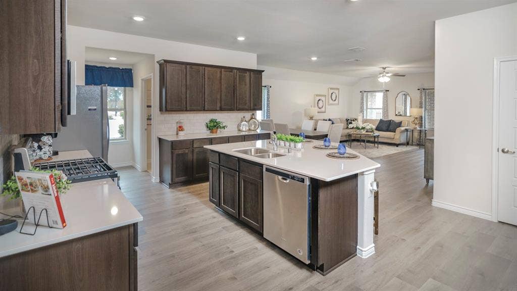 406 Campfield Drive, Caddo Mills, TX 75135 Contemporary kitchen featuring wood-finish cabinetry, light-toned countertops, stainless steel appliances, and a central island with an integrated sink