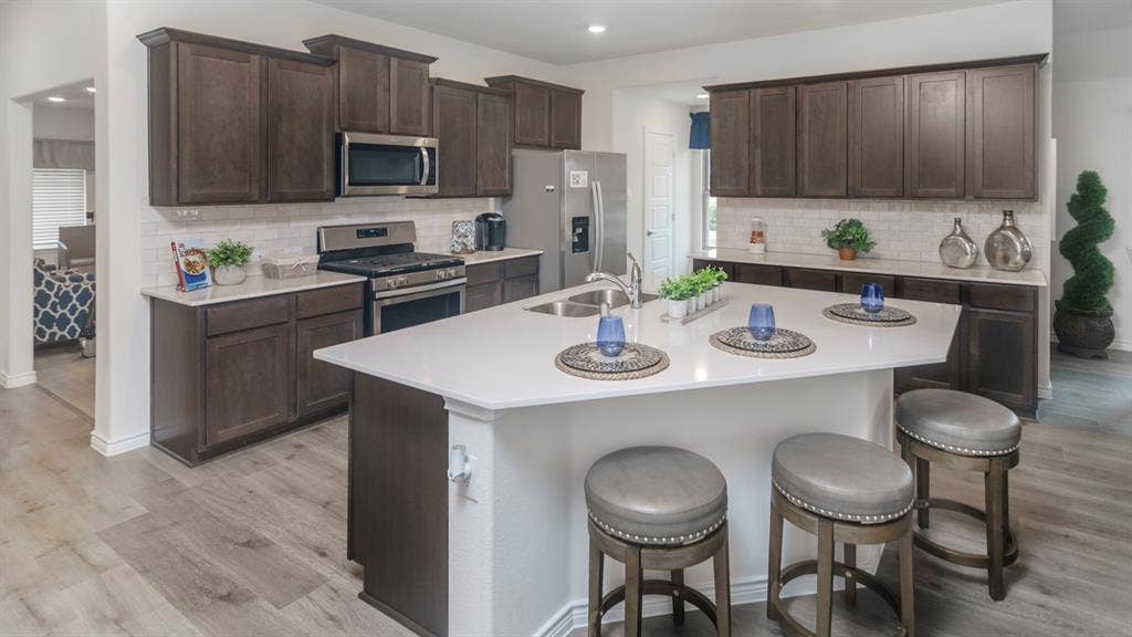 406 Campfield Drive, Caddo Mills, TX 75135 Kitchen featuring a central island with countertop seating, wood-finish flooring, dark wood cabinetry, white subway tile backsplash, and stainless steel appliances