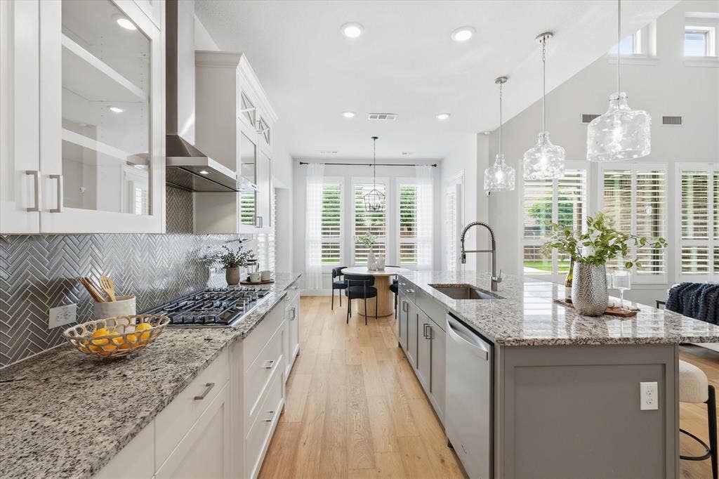 A crisp, clean kitchen featuring bright white ceiling-height cabinetry, double ovens, a gas stove, a walk-in pantry, and an adjoining sunlit breakfast nook.