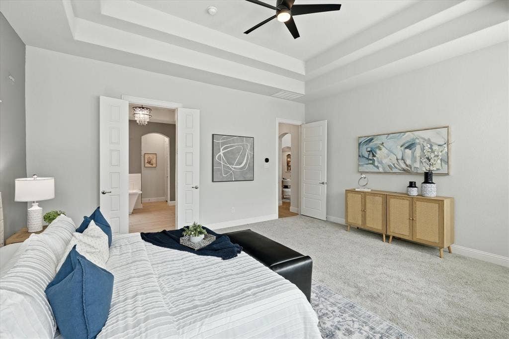 Spacious primary bedroom featuring a tray ceiling, expansive bay windows with plantation shutters, and reading area.