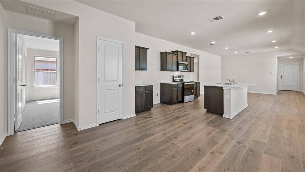 Open-concept living area featuring wood-finish flooring, recessed lighting, and a kitchen with dark cabinetry and a center island with a sink