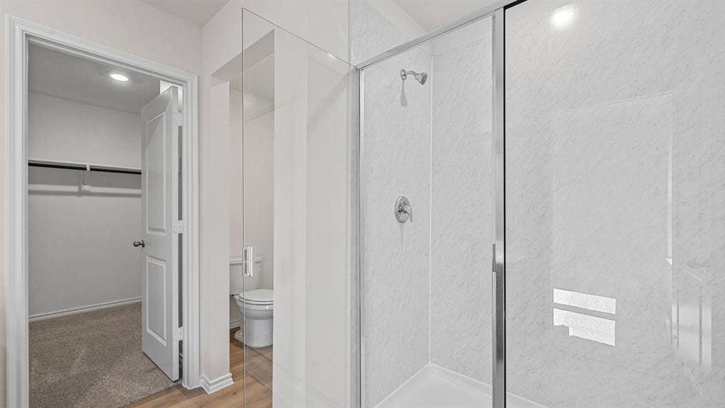 Glass-enclosed shower with a chrome showerhead, white shower surround, and matching chrome fixtures